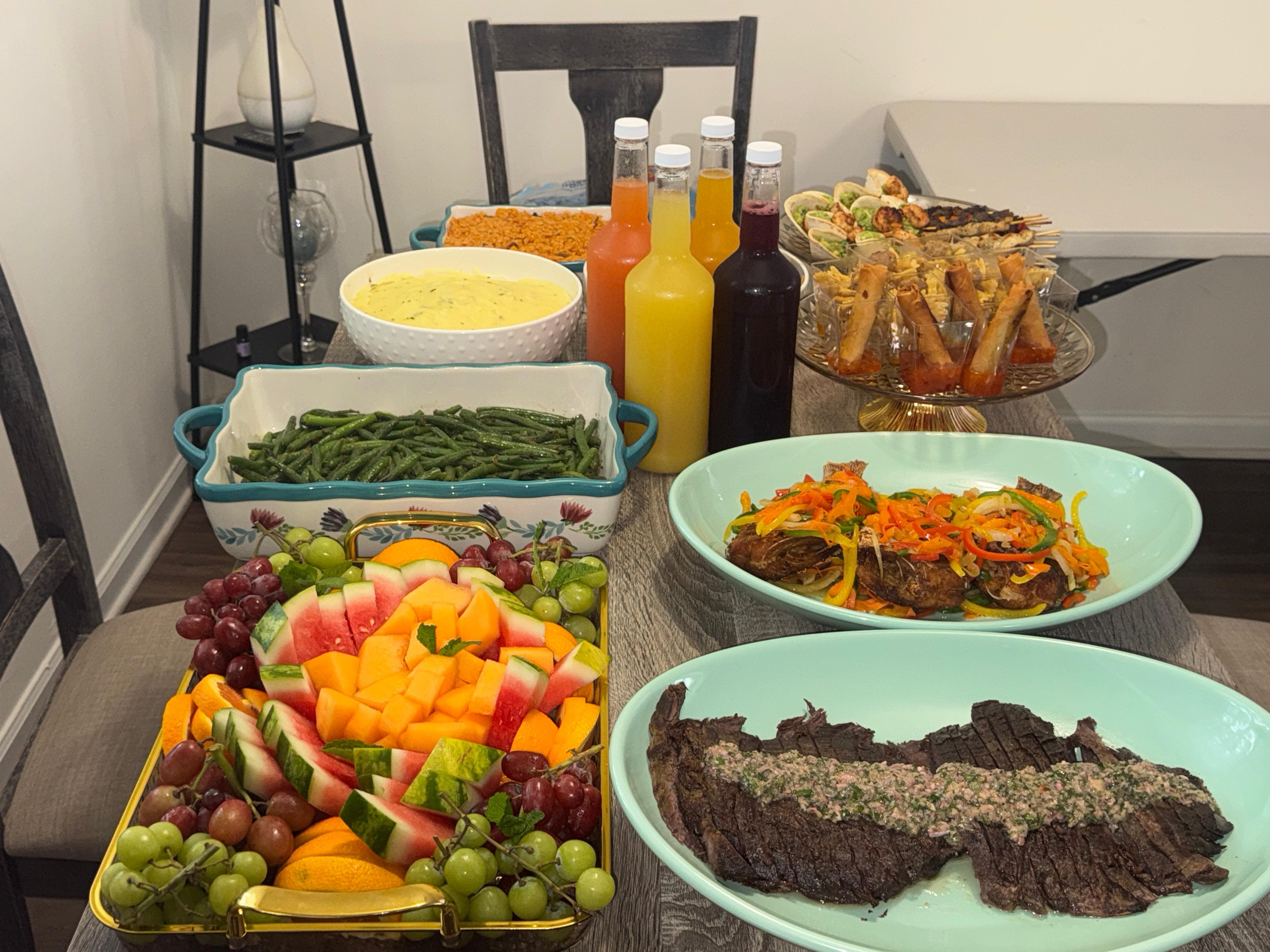 Full catering spread with grilled steak, spring rolls, fruit platter, and more